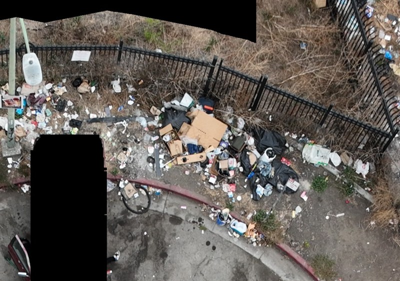Loose debris and bulky dumped items beside a curved sidewalk and metal fence