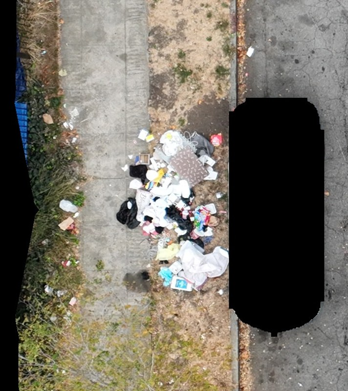 Mixed dumped waste beside the curb, with a vehicle redacted